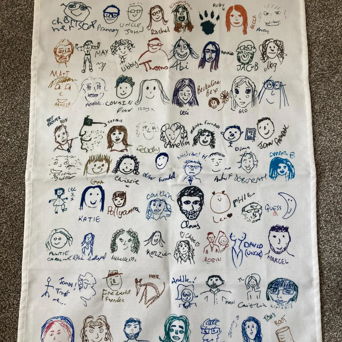 Cream tea towel printed with colourful hand-drawn guest self-portraits